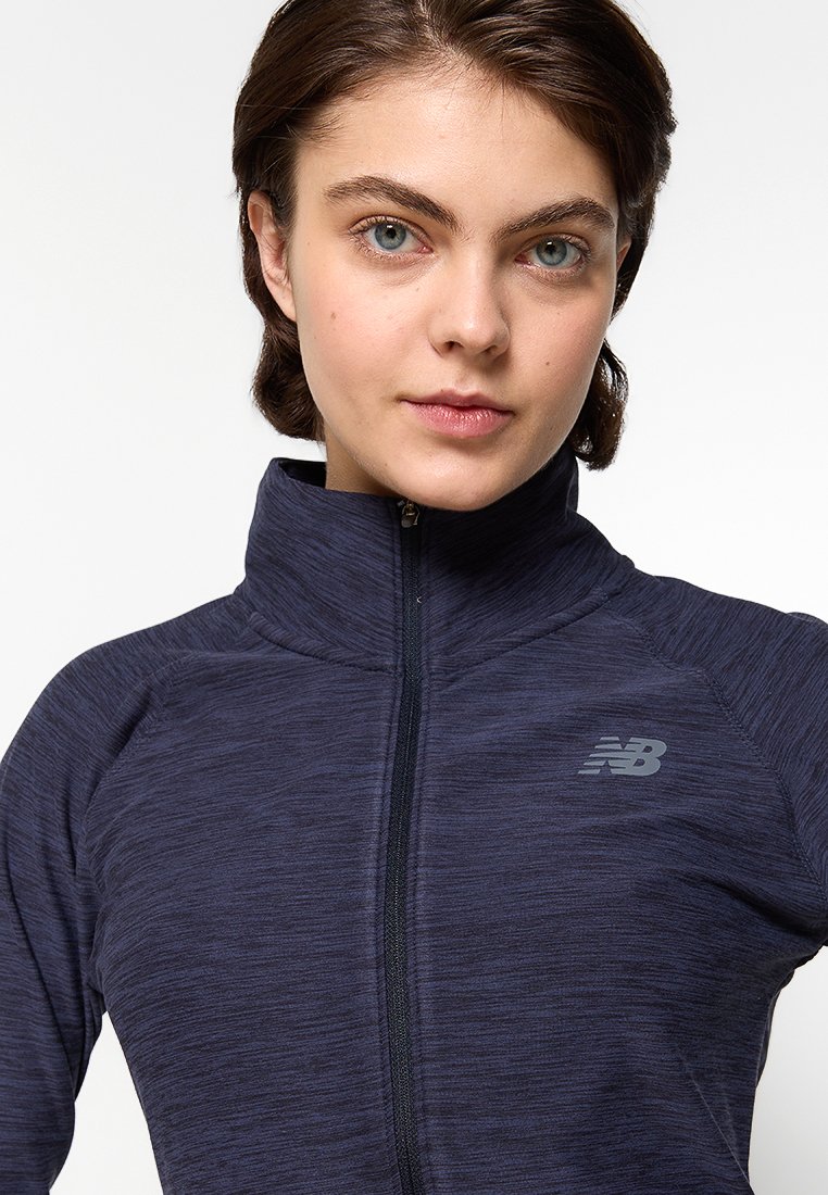 Chaqueta con cremallera en navy de una tela texturizada. Presenta un alto cuello y el logo reflectante de New Balance en el lado izquierdo del pecho.