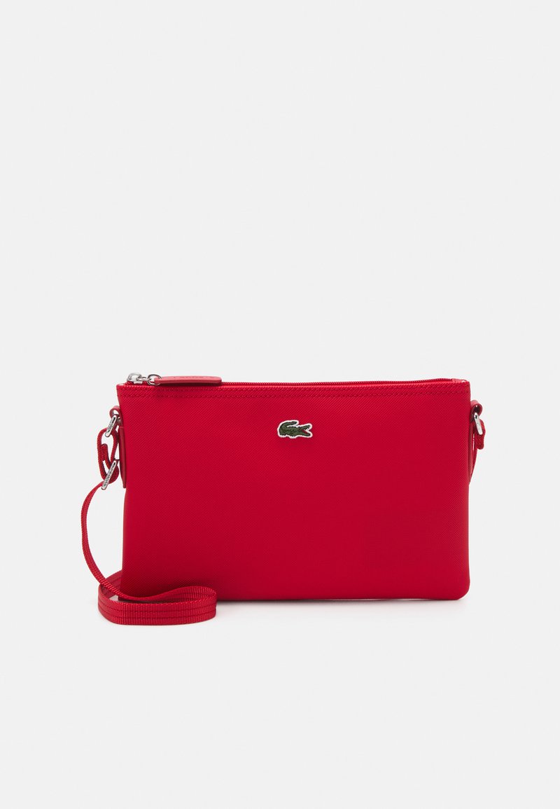 Borsa a tracolla sintetica rossa con chiusura a zip, caratterizzata da un piccolo logo verde e una tracolla rimovibile. Texture liscia, forma rettangolare.
