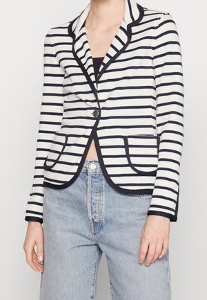 Personne portant un blazer rayé blanc et marine avec une bordure noire, un bouton fermé, associé à un jean taille haute bleu clair.