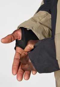 Μανίκι μπεζ και μαύρου υφασμάτινου σακακιού με εφαρμοστή μαύρη εσωτερική επένδυση. Ένα χέρι είναι περασμένο στο μανίκι, προβάλλοντας το υλικό και το σχεδιασμό.