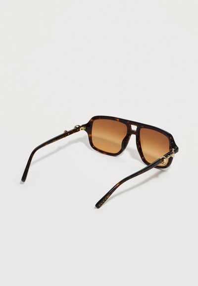 Γυαλιά ηλίου ορθογώνια με σχέδιο χελώνας, φακούς καφέ με διαβάθμιση και χρυσές λεπτομέρειες, ανοιχτά πάνω σε ανοιχτή επιφάνεια.