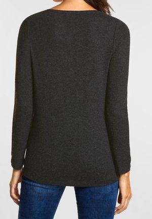 Kvinde iført en ensfarvet mørkegrå langærmet sweater sammen med blå jeans, vist bagfra mod en ensfarvet baggrund.