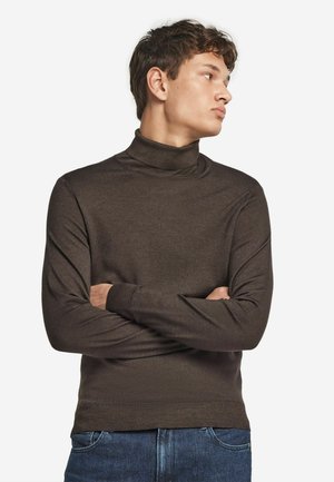 Brązowy sweter typu golf wykonaný z gładkiej dzianiny, z długimi rękawami i dopasowanym krojem, zestawiony z niebieskimi dżinsami.