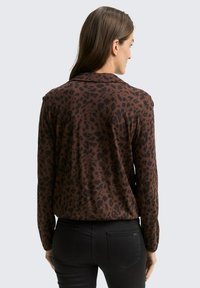 Bruine blouse met luipaardprint, lange mouwen, een kraag en een relaxte pasvorm. Zacht materiaal met opvallende donkere vlekken op een lichtere bruine achtergrond.