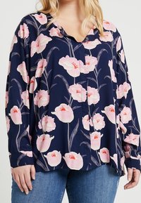Blusa floreale con sfondo blu navy, caratterizzata da motivi di fiori rosa e bianchi, maniche lunghe e chiusura con bottoni.