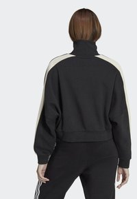 Felpa nera accorciata con colletto alto, caratterizzata da pannelli laterali crema e polsini a costine. Tessuto morbido con una vestibilità rilassata e design minimalista.
