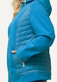 Blå jacka med kviltad design på framsidan, med dragkedjesl closure och huva. Slät textur och en förlängd form med sidofickor.