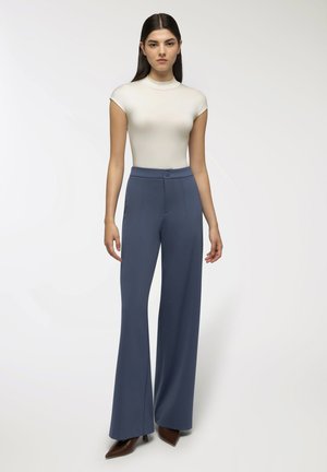 Top fitted beige chiaro con maniche a cappuccio abbinato a pantaloni a vita alta blu navy svasati con bottone frontale e dettagli delle tasche.