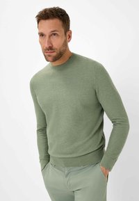 Hellgrüner Strickpullover mit rundem Halsausschnitt, langen Ärmeln und gerippten Akzenten an den Bündchen und dem Saum, kombiniert mit hellgrünen Hosen.