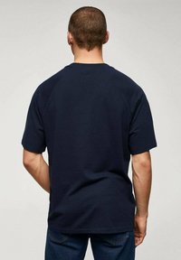 Navy modrá bavlněná tričko, krátké rukávy, kulatý výstřih, volný střih. Hladká textura s jednoduchým designem, bez viditelných log nebo vzorů.