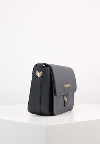 Black leather crossbody bag with a structured design, gold-tone hardware, and a prominent logo. Features a flap closure and geometric accents.