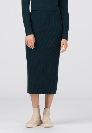 Strikket midi-nederdel i mørk teal med ribbet struktur, kombineret med beige ankelstøvler med glat finish og sidesyningsdetaljer.