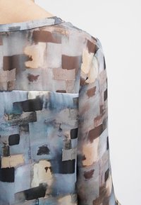Blusa di seta con motivo geometrico in tonalità di blu, marrone e crema, con una texture liscia e una vestibilità comoda.