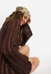 Καφέ πλεκτό φόρεμα με φαρδιά μανίκια και κάθετες ρίγες, με ανοιχτό πλέξιμο. Διακοσμημένο με φουλάρι λεοπάρ σε μπεζ και καφέ αποχρώσεις.