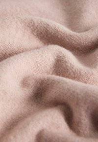 Hele roosa kangas, millel on pehme, tekstuuriga pind ning õrnad lained ja voldid, mis viitavad mugavale fliis- või villa materjalile.