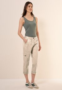 Lichtgroen tanktop gecombineerd met beige cropped cargobroek met zijzakken en opgerolde hemden, aangevuld met neutrale sneakers.