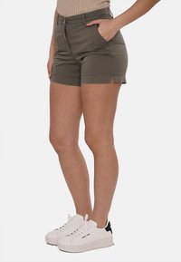 Pantaloni corte verde oliva dal design aderente, con tasche frontali, spacchi sull'orlo e una texture liscia, abbinati a sneakers bianche.