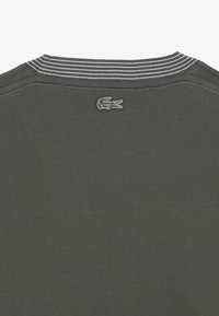 Donkergroene katoenen T-shirt met een gestreepte ribboord en geborduurd krokodillenlogo op de rug. Zachte textuur, casual ontwerp.