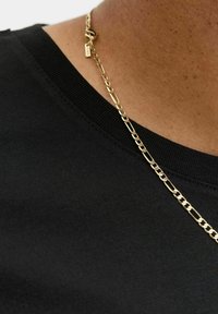 Schwarzes T-Shirt mit geripptem Halsausschnitt, kombiniert mit einer goldenen Kettenhalskette mit verlängerten Gliedern und einem Verschluss.