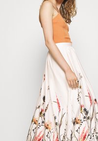 Lång, flödande kjol i ljusrosa med blommigt akvarelltryck. Figursydd topp i ribbad orange tyg. Mjuk textur och design med hög midja.