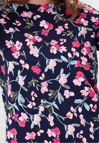 Námořnický top s květinovým vzorem s růžovými a světle modrými květy, strukturovaný s kulatým výstřihem a krátkými rukávy. Hladká textura látky.