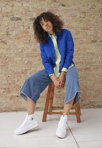 Veste bleu à boutons sur une chemise à rayures vertes et blanches, associée à des culottes en denim à jambes larges et des baskets montantes blanches.