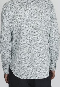 Vit skjorta med lång ärm och ett grönt blommönster. Har knappade manschetter och en böjd nederkant. Tyget verkar lätt och texturerat.