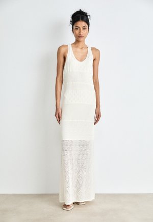 Langes, ärmelloses weißes Kleid mit einem gemusterten Häkeldesign, einem taillierten Oberteil und schwingenden unteren Teilen. Strukturierter Strickstoff.