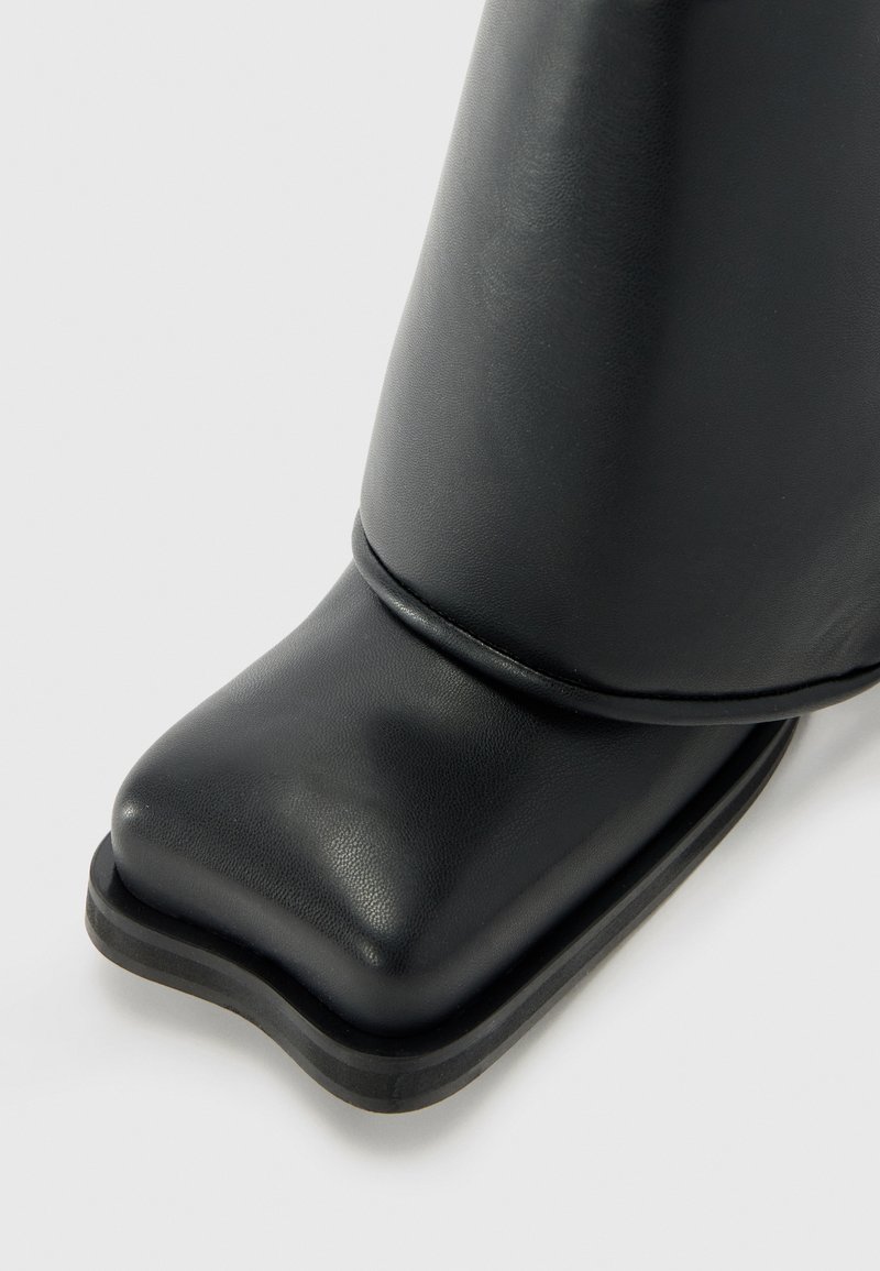 Stivale alla caviglia in pelle nera con texture liscia, punta quadrata e suola spessa in gomma nera. Presenta un design cucito all'altezza della caviglia.