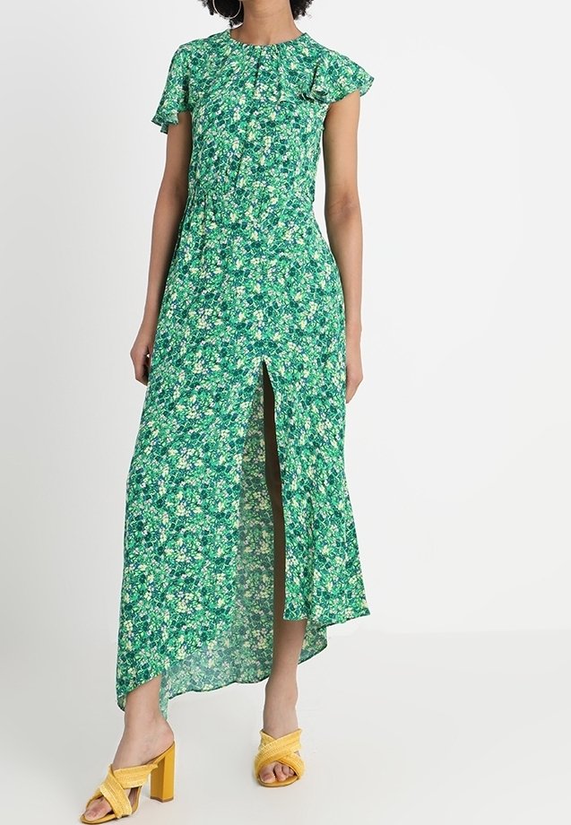 Grön blommig maxiklänning med korta volangärmar, hög sprund och en flödande design. Accenterad med gula klacksandaler.
