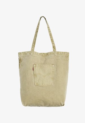 Beige lærredstaske med to håndtag og en frontlomme med en lille rød mærkat på en hvid baggrund.