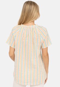 Blusa a maniche corte a righe con colori pastello (rosa, verde, giallo) con arricciature al collo e orlo curvo. Tessuto leggero.