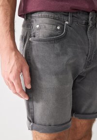 Shorts en denim gris avec un ourlet retourné, dotés de poches avant et d'accents en métal argenté. Le tissu a une texture douce et usée.