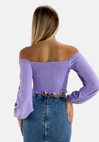 Crop top lilas à épaules dénudées avec texture smockée et ourlet volé. Doté de longues manches amples et d'une coupe ajustée, associé à une jupe en denim taille haute.