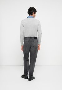 Camisa cinza de manga longa com colarinho azul claro, combinada com jeans cinza escuro. Sapatos pretos. Detalhes visíveis nas costas incluídos os bolsos e a cintura.