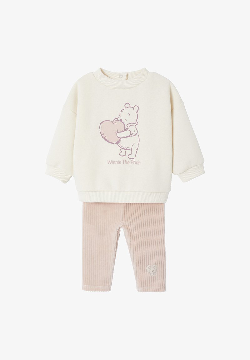 Cremfarbener Pullover mit einem pinken "Winnie the Pooh"-Grafikmotiv, kombiniert mit hellrosa, gerippten Leggings, die ein Herzdesign am Bein aufweisen.