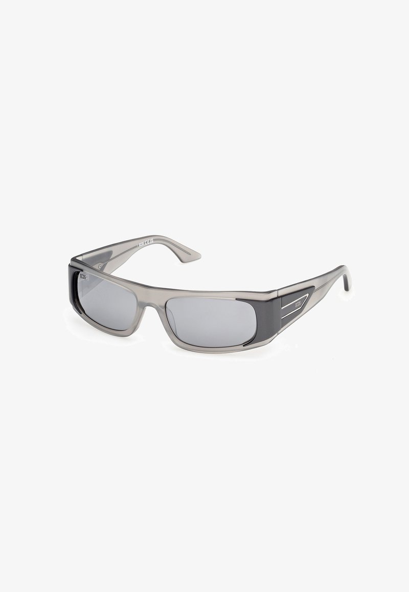 Lunettes de soleil rectangulaires gris fumé avec des accents noirs sur les branches et des verres teintés foncés, inclinées sur un fond blanc.