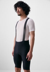Shorts de cyclisme noirs avec un rembourrage, associés à un tee-shirt en mesh blanc ajusté avec des bretelles noires. Le matériau semble léger et respirant.
