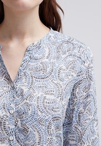 Leichte, weißer Hemd mit Knopfleiste, versehen mit einem blau-schwarzen farnartigen Muster. Weicher Stoff mit einem Kragen und drei Knöpfen.