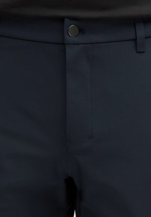 Tmavomodré na mieru šité nohavice majú hladkú látku, rovný predný diel a kovové zapínanie na páse.