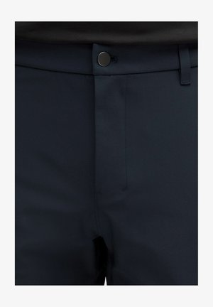 Tmavomodré na mieru šité nohavice majú hladkú látku, rovný predný diel a kovové zapínanie na páse.