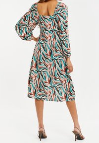 Robe multicolore avec un dos carré, des manches bouffantes et un motif ondulé en turquoise, rouge, noir et crème. Design mi-long.