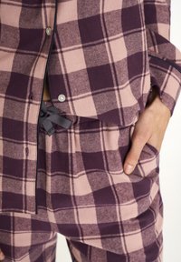 Pink and purple checkered loungewear set featuring a button-up top and elastic waistband pants. Soft fabric with a relaxed fit and pockets.