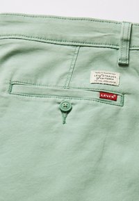 Jasnozielone spodnie z tylną kieszenią zapinaną na zielony guzik, metka Levi's i kontrastującym czerwonym logo. Miękka tekstura materiału.