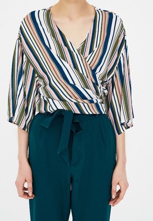 Femme portant un chemisier portefeuille rayé multicolore avec des manches au coude et un pantalon taille haute bleu sarcelle noué avec une ceinture en tissu.