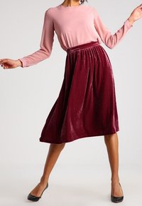 Burgundy sammet midi kjol med elastisk midjeband, ihop med en ljusrosa långärmad blus och svarta flata skor.