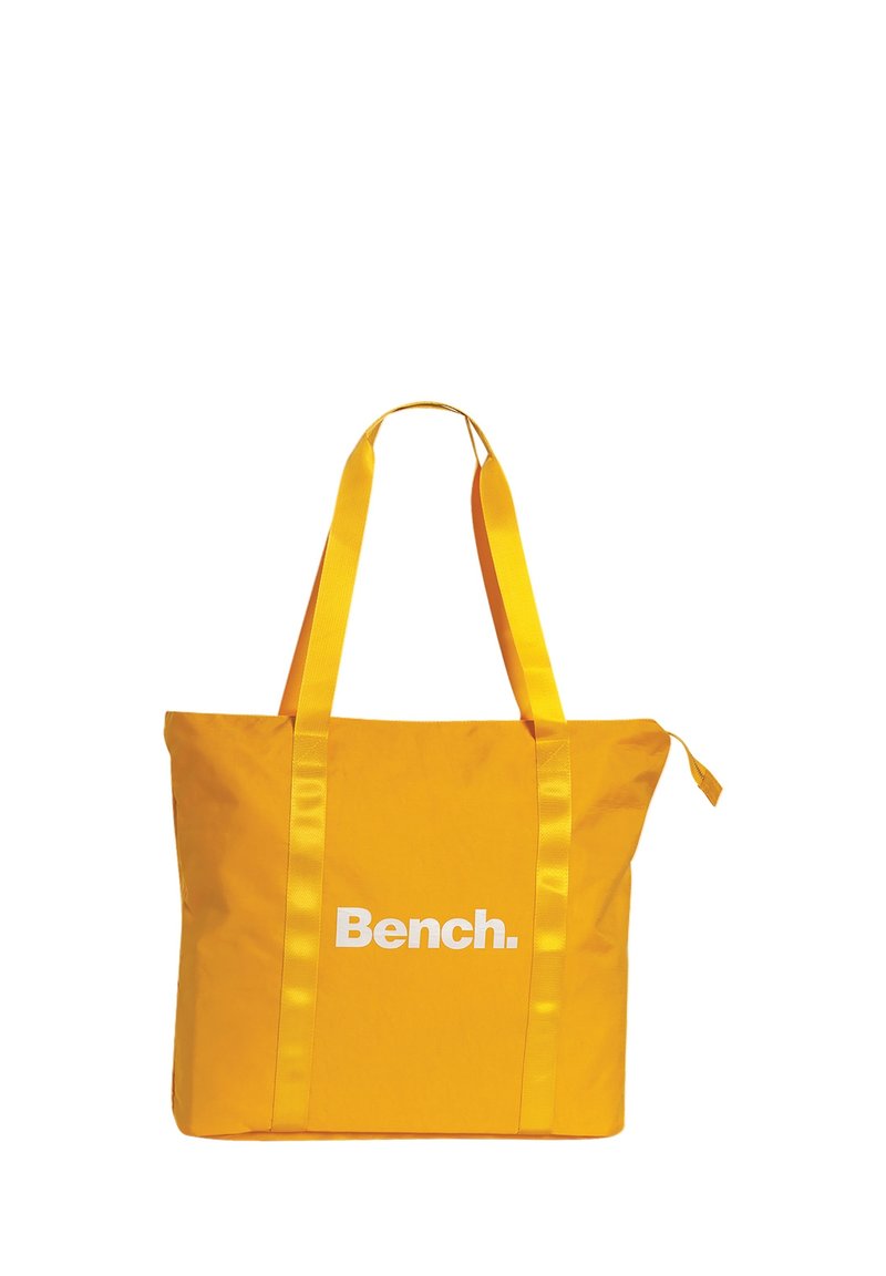 Gele boodschappentas met satijnen banden en een wit logo "Bench." aan de voorkant, met een gladde textuur en een ruim ontwerp.