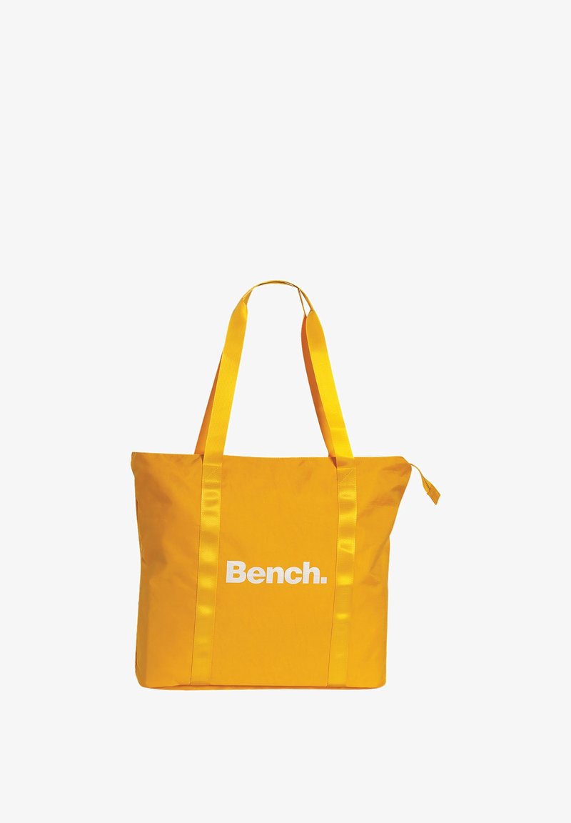 Gele boodschappentas met satijnen banden en een wit logo "Bench." aan de voorkant, met een gladde textuur en een ruim ontwerp.