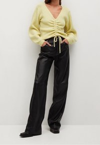 Pull tricot jaune à col en V et devant froncé, associé à un pantalon large en cuir noir. Le pull présente un détail de cordon de serrage.