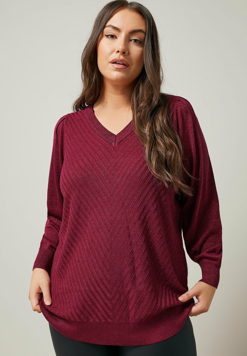 Pull bourgogne avec un col en V, présentant un motif en chevrons et des manches longues. Fabriqué en tricot texturé, avec des poignets et un ourlet côtelés.